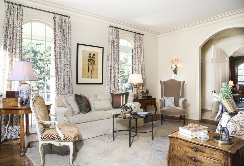 Arched doorways are echoed in the living room’s windows, framed by Fortuny-esque drapes. “The arches were one of my favorite things when we first saw this house,” says Kyler. The Régence iron coffee table is a find from Fireside Antiques, while many of the other furnishings throughout the house were procured through Dixon Smith Interiors.